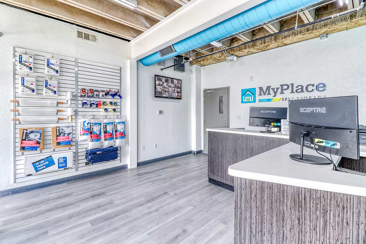 MyPlace Self Storage Dallas office interior featuring moving supplies for sale and live security monitoring screens.